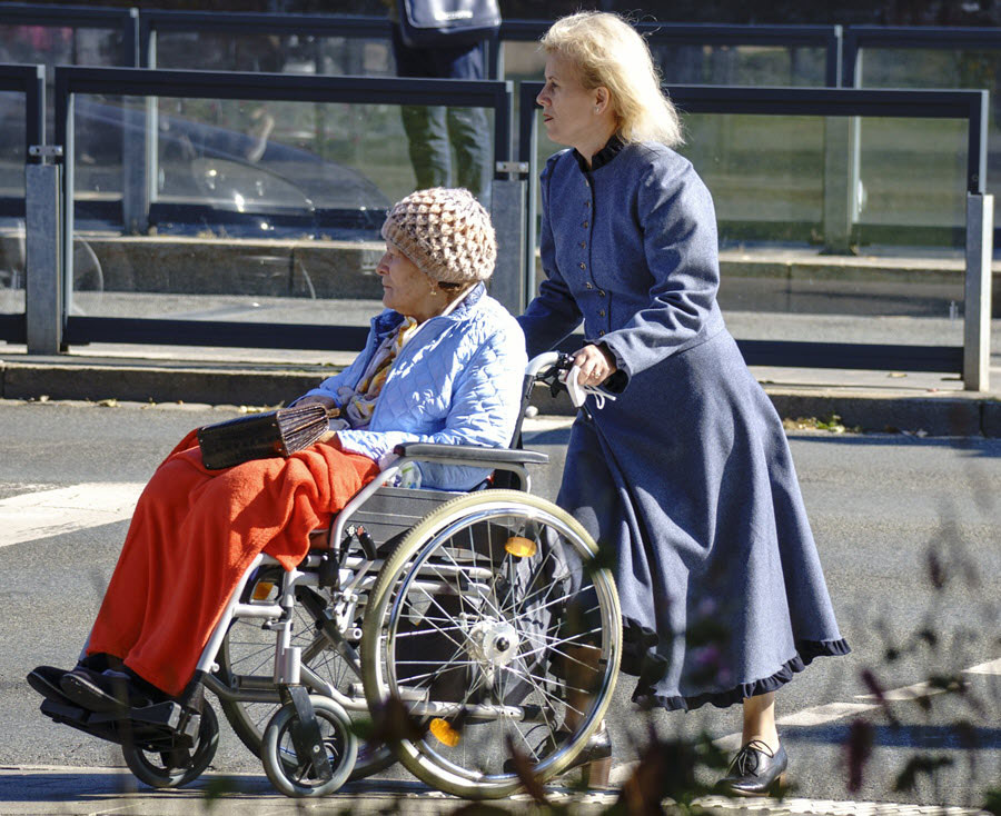 elderly woman in a wheelchair being guided down the street